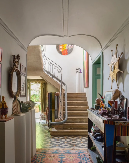View of an interior hallway and staircase, featuring decorative objects, artwork, and patterned flooring, creating a vibrant and artistic home space.