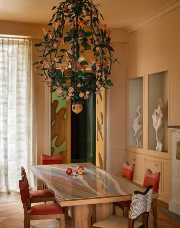 Eclectic dining room interior with a wooden table, red chairs, and a decorative floral chandelier hanging overhead, next to a doorway.