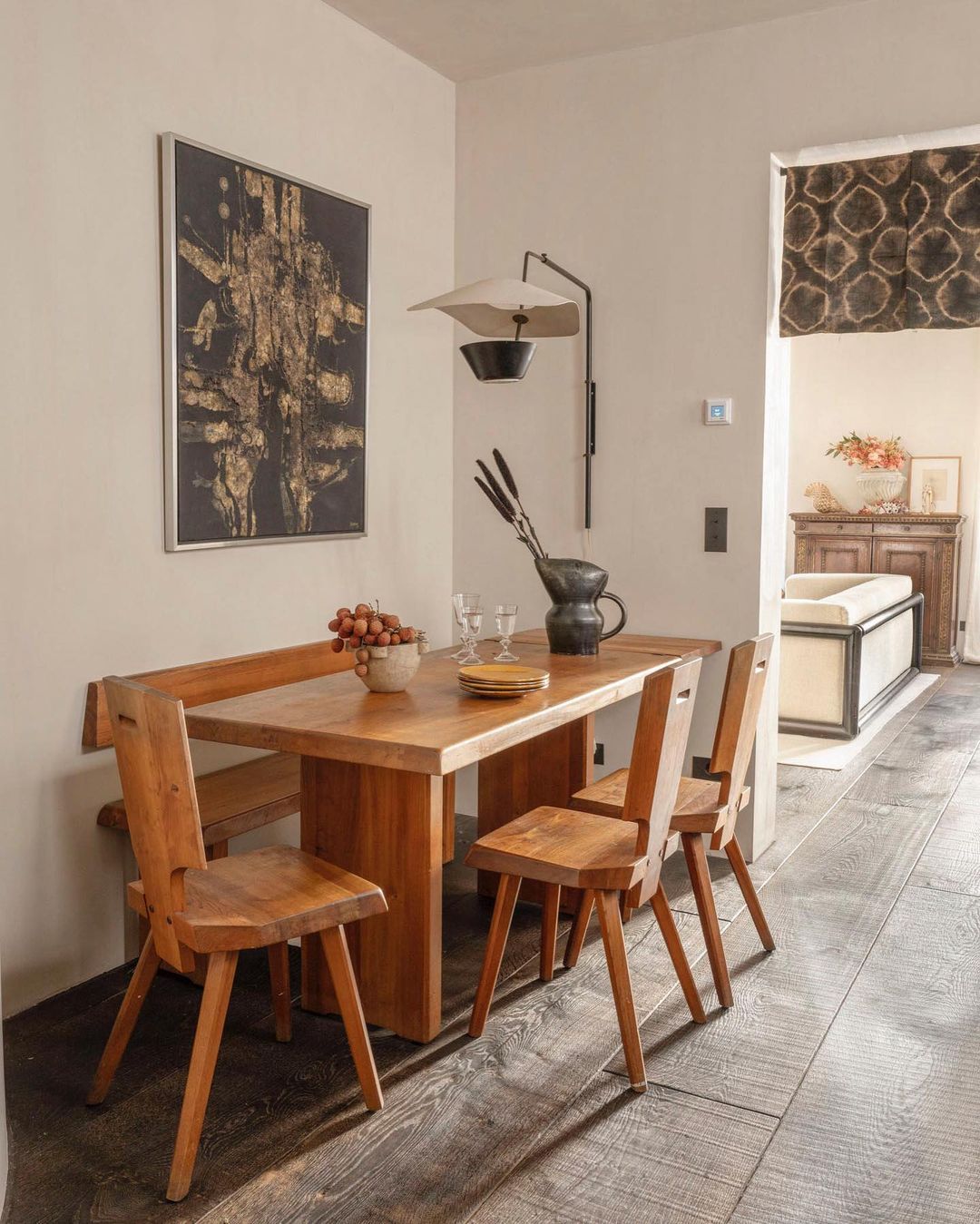 Warm, rustic interior design showcasing a wooden dining table with chairs, complemented by a unique wall lamp and abstract art.