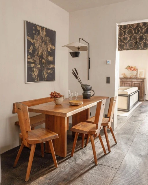 Warm, rustic interior design showcasing a wooden dining table with chairs, complemented by a unique wall lamp and abstract art.