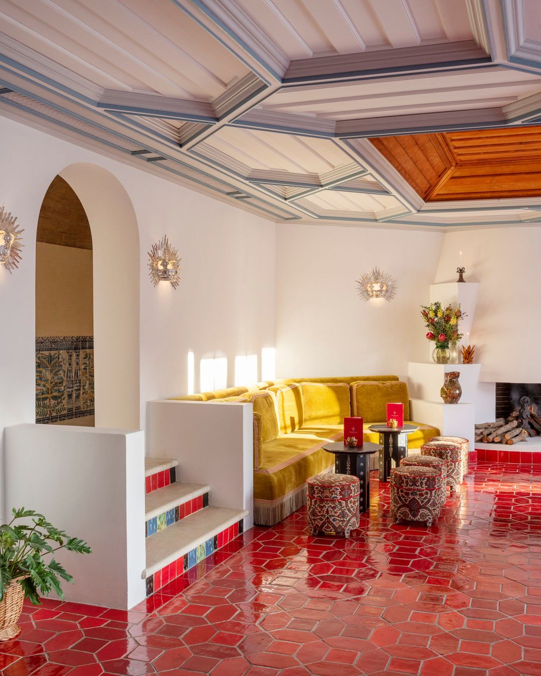 Interior space features yellow sectional sofa, patterned ottomans, round tables, fireplace, and detailed ceiling design.