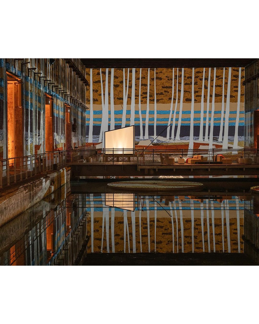 Interior view of The Turbine Hall at Tate Modern museum in London with a reflective pool and an art installation backdrop.