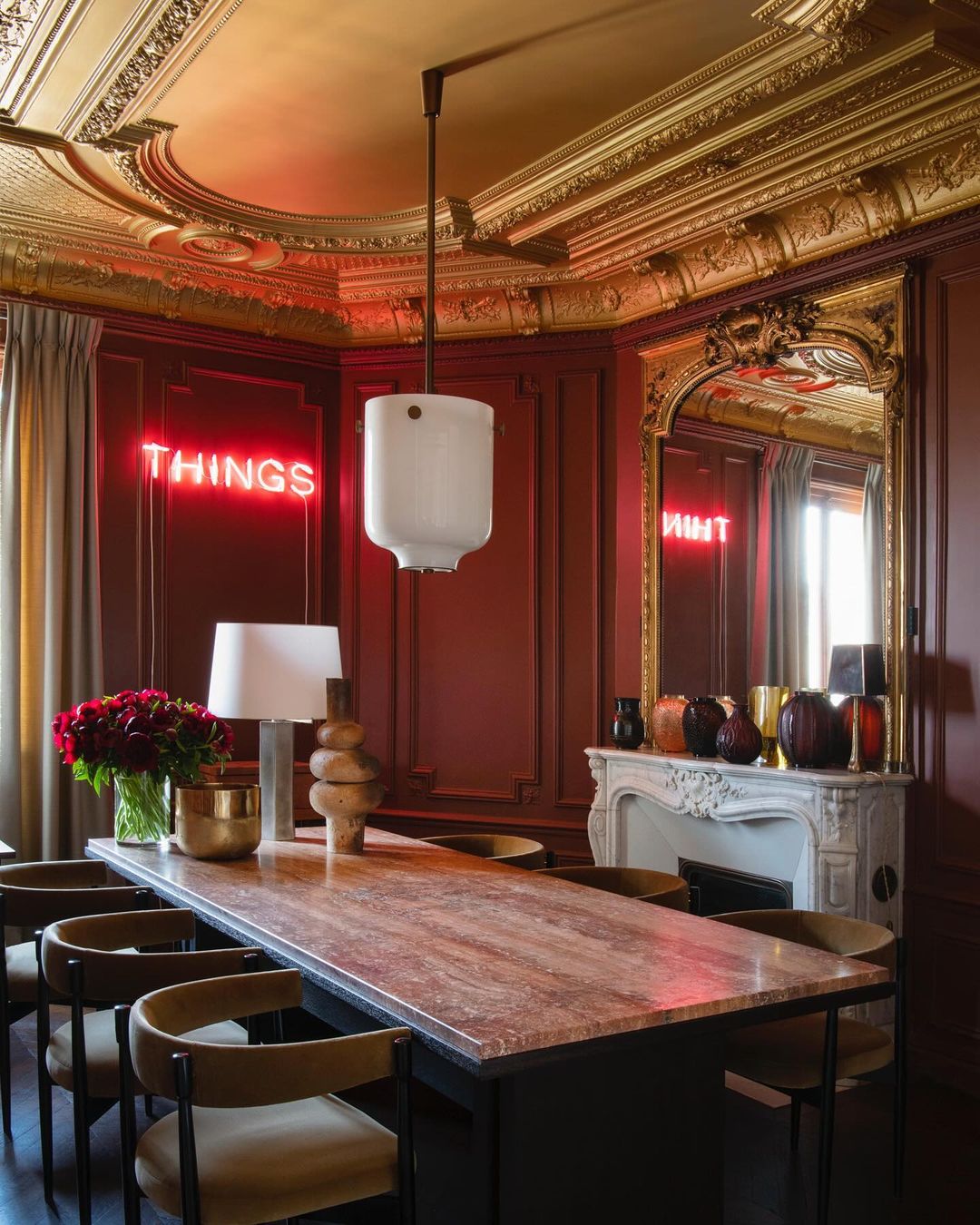 Ornate interior dining room featuring a long table, chairs, modern pendant light, and red neon sign in a room with decorative moulding.