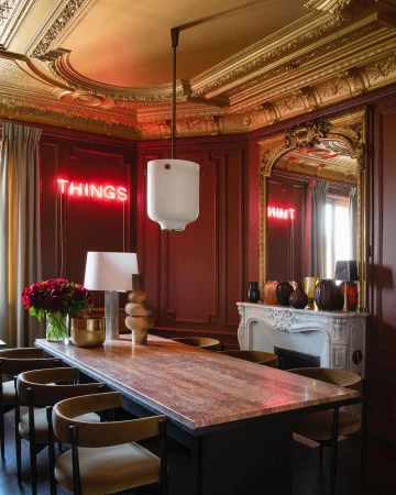 Ornate interior dining room featuring a long table, chairs, modern pendant light, and red neon sign in a room with decorative moulding.