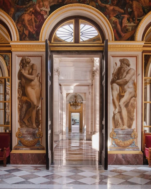 Architectural shot inside a long hallway, adorned with classical statues, marble floors, and mural paintings, evoking a sense of grand elegance.