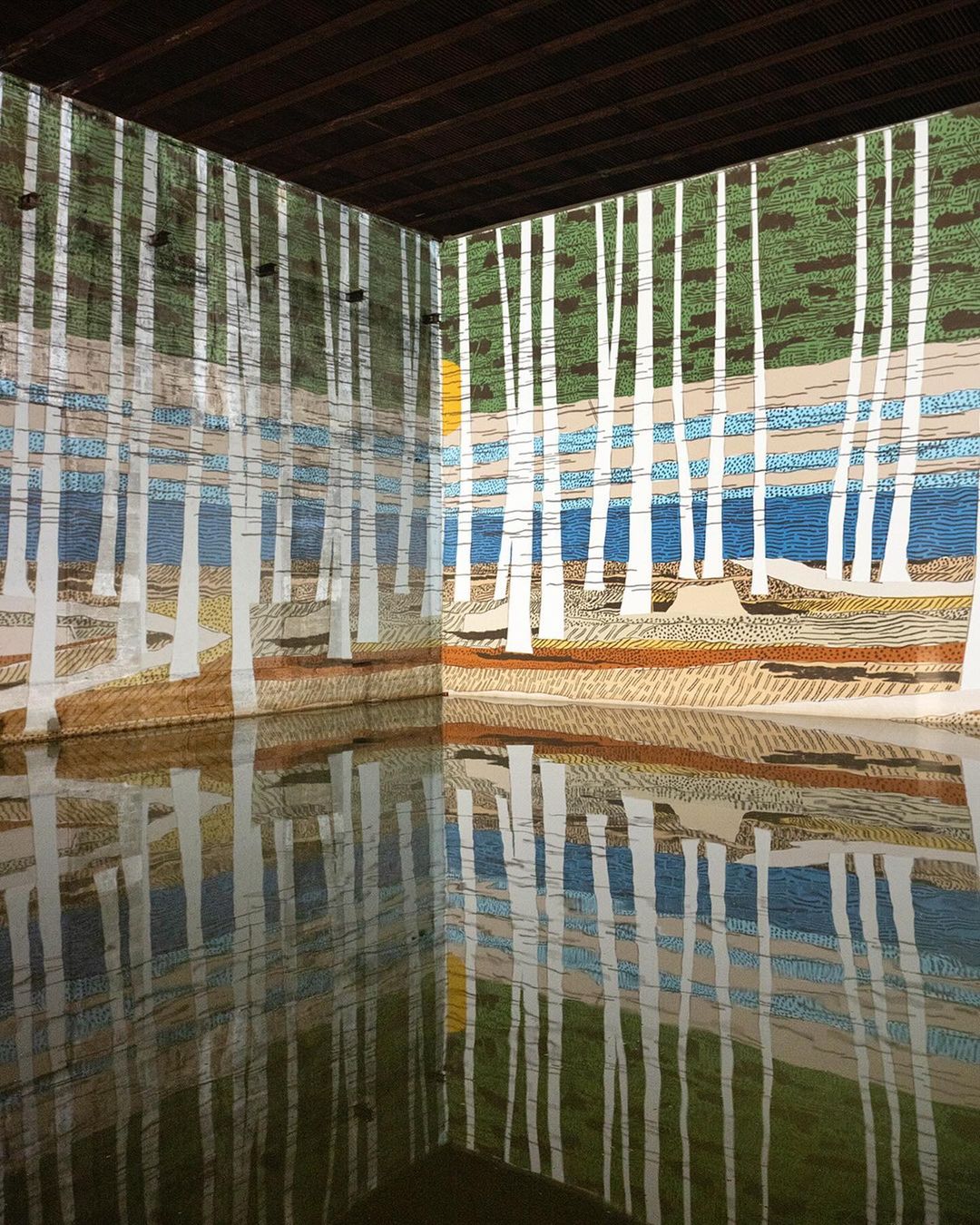 Painted forest landscape art installation in an indoor space, reflected on the floor. Abstracted trees and water create a serene scene.