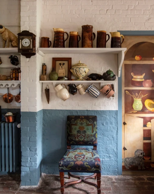 A vintage-styled interior with a chair in front of shelves displaying ceramic pitchers and dishware, creating a cozy, collected aesthetic.