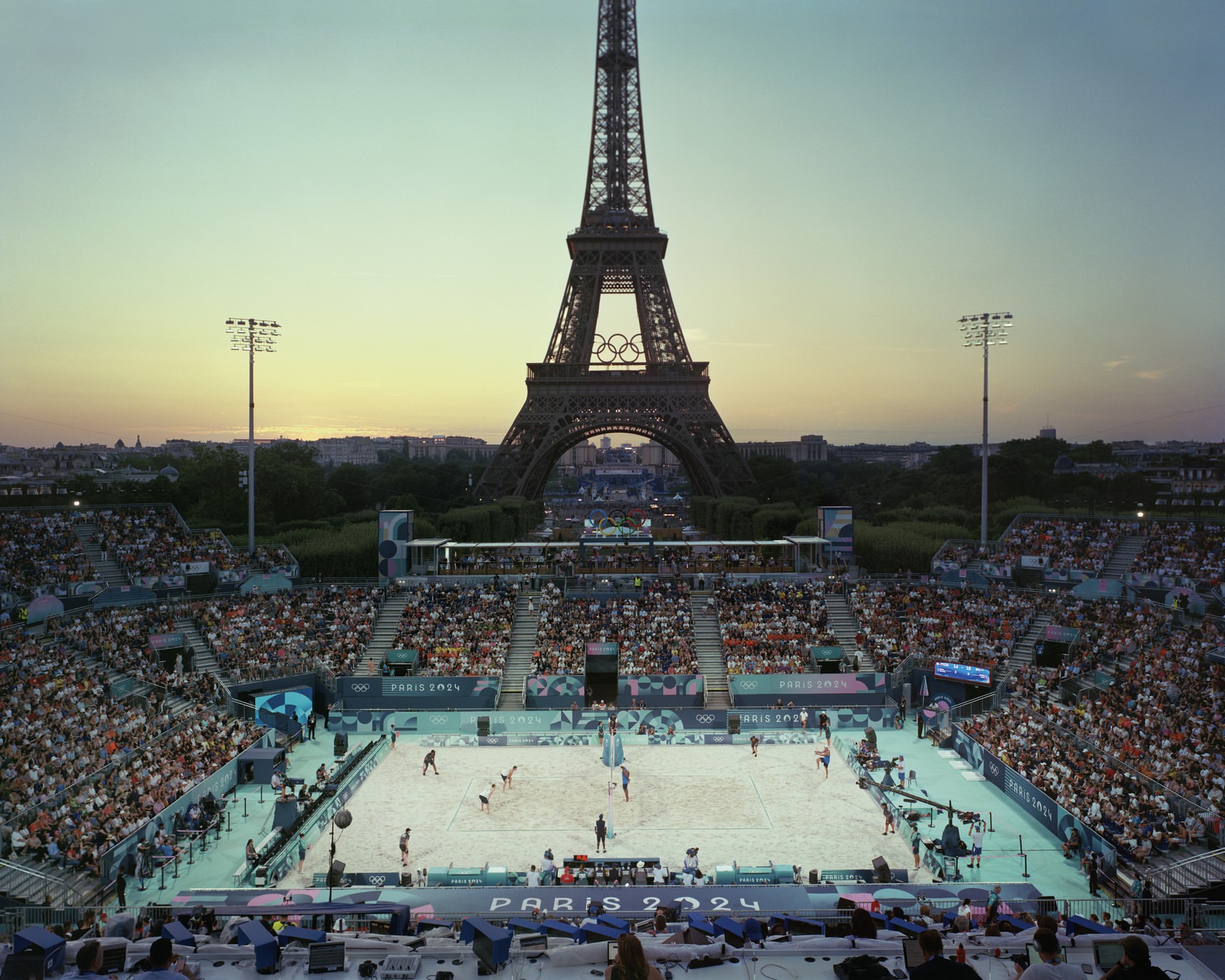 Eiffel Tower in Paris, France, serves as a backdrop to a beach volleyball game in a stadium packed with spectators at dusk.