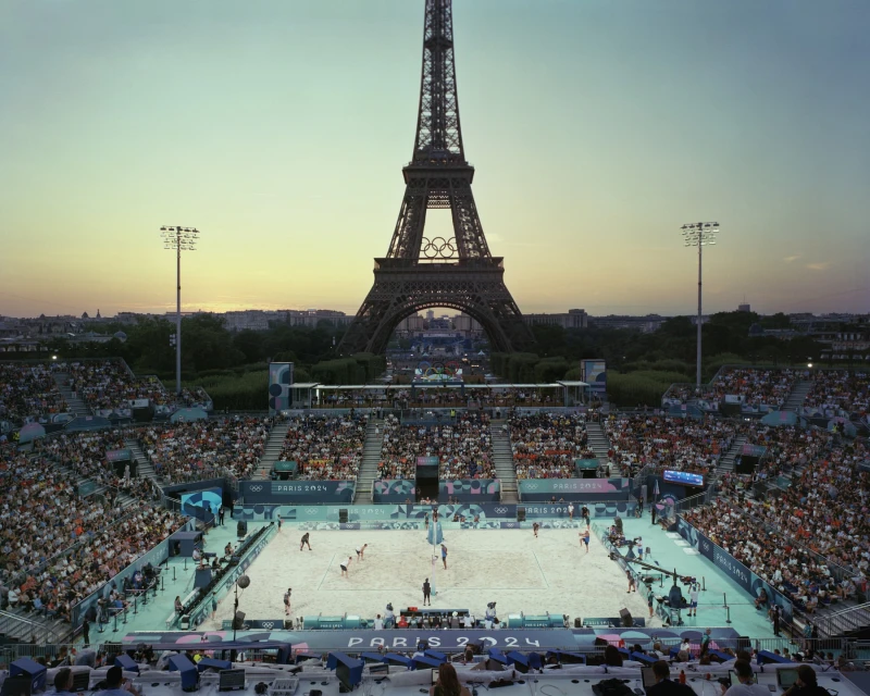 Eiffel Tower in Paris, France, serves as a backdrop to a beach volleyball game in a stadium packed with spectators at dusk.