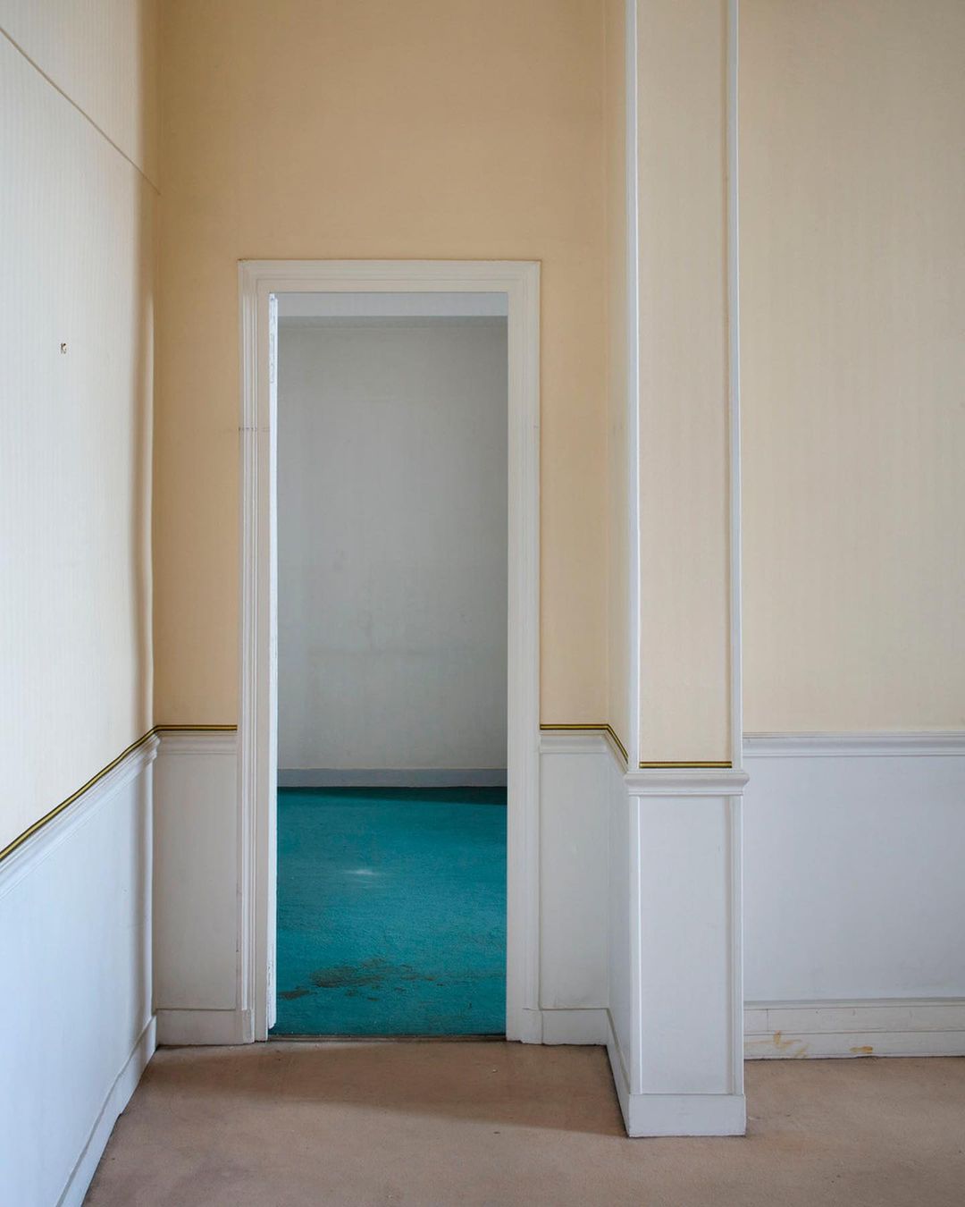 Empty room interior featuring beige walls, white trim, and a doorway leading to a room with a contrasting blue floor.