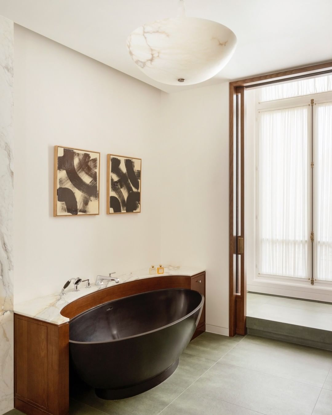 A modern bathroom featuring a dark freestanding bathtub, white marble countertops, and abstract artwork, illuminated by a ceiling light.