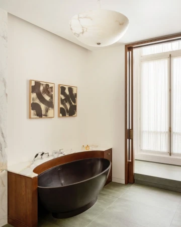A modern bathroom featuring a dark freestanding bathtub, white marble countertops, and abstract artwork, illuminated by a ceiling light.