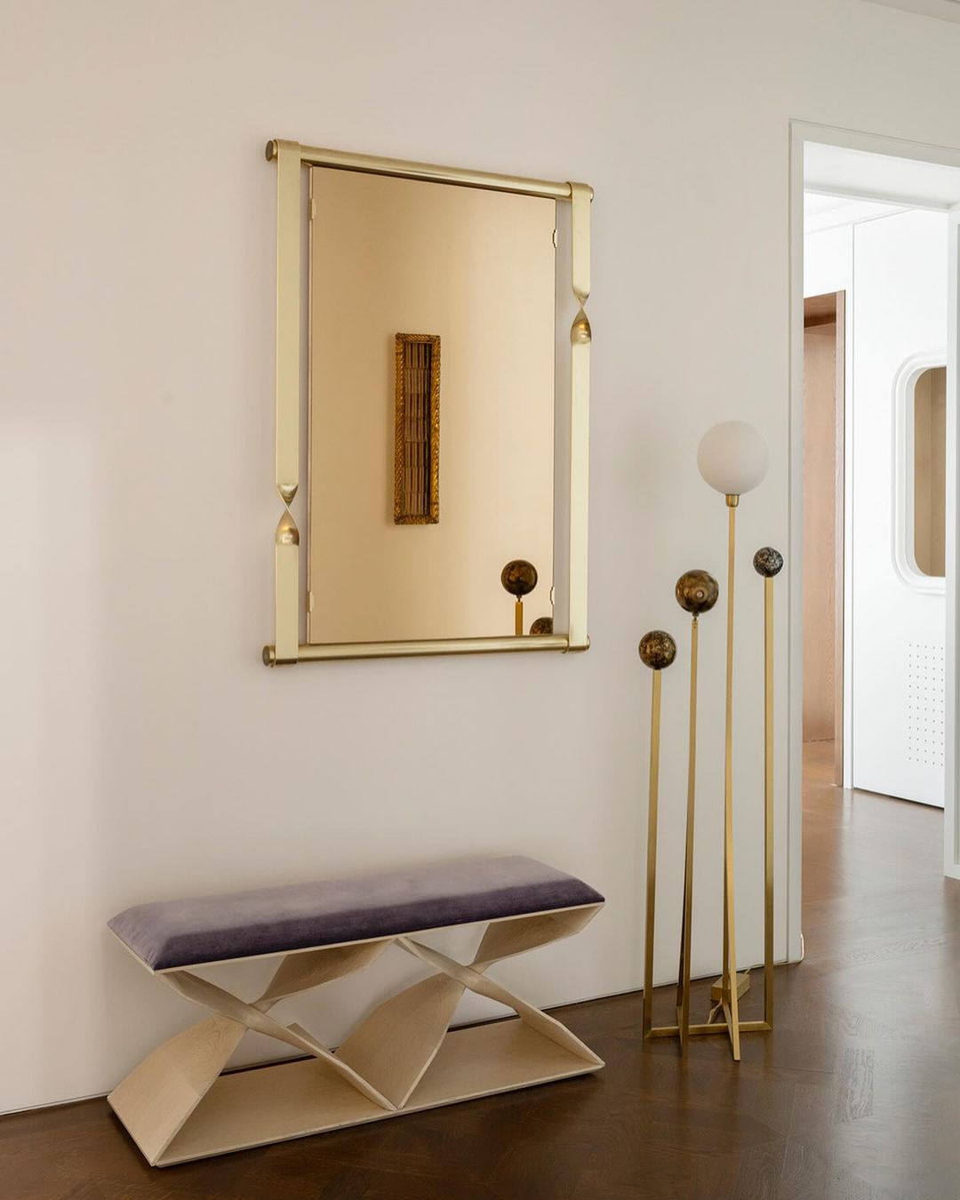 Interior design of hallway with beige walls featuring a framed mirror, decorative floor lamps, and a bench with purple velvet upholstery.