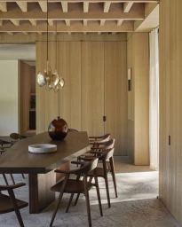 Modern wooden dining room interior featuring a long dark wood table, matching chairs, and brass pendant lights.
