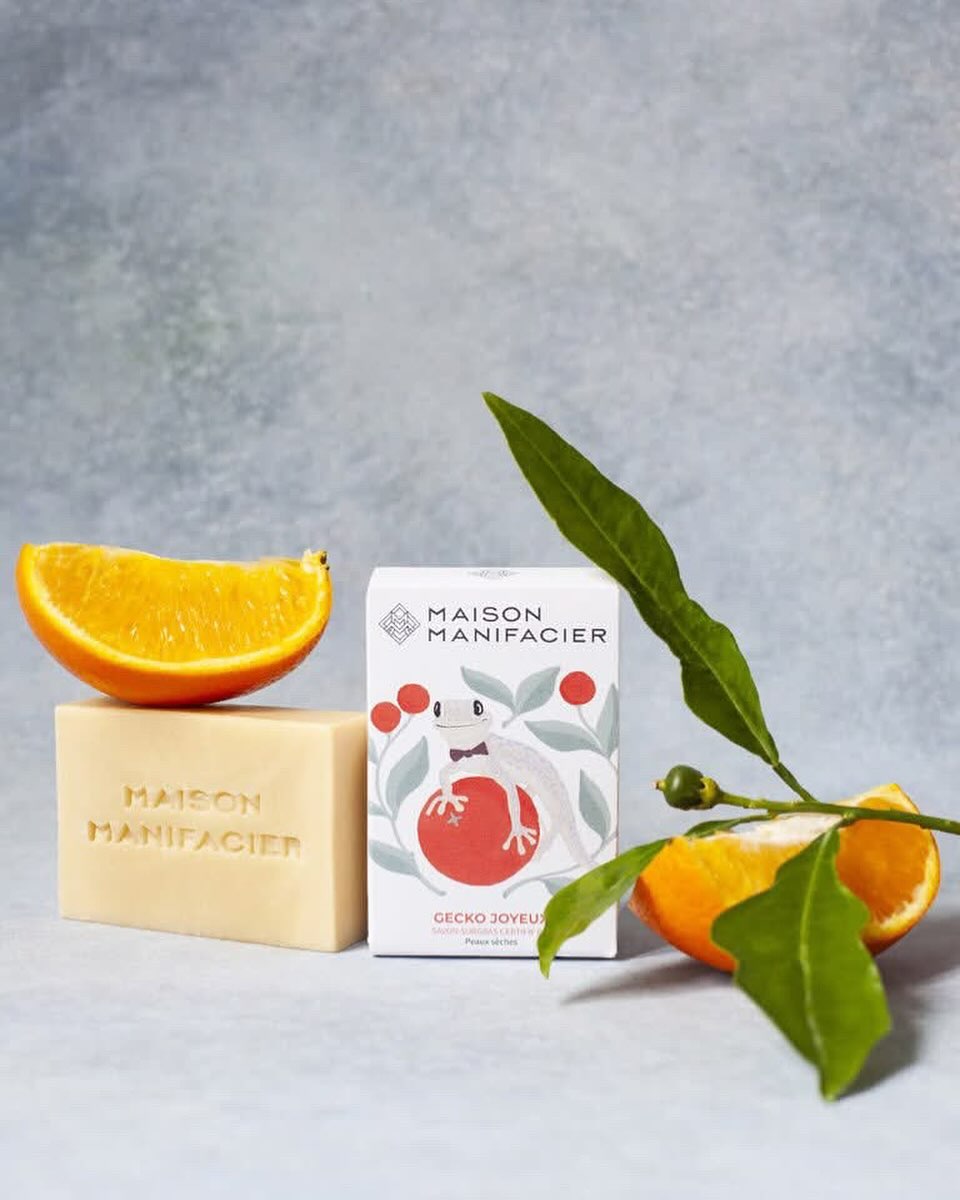Still life of artisan soap, orange slices, and leafy sprig against a mottled gray background, showcasing natural ingredients and textures.