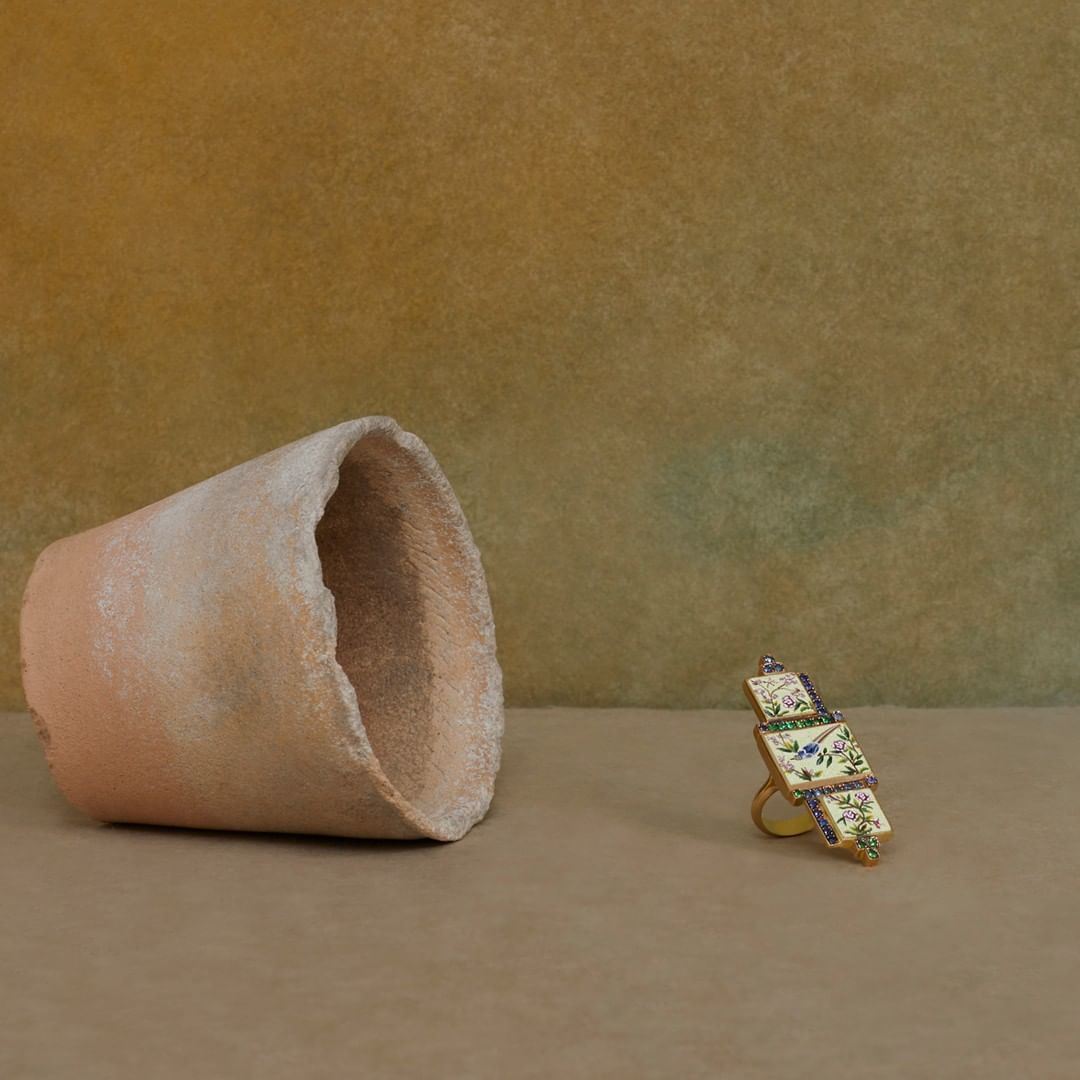 Still life featuring a terracotta pot lying on its side and a ring with floral design against a textured, neutral background.