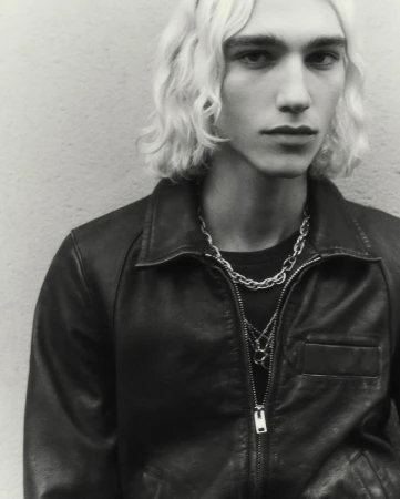 Portrait of a young man with wavy blonde hair wearing a black leather jacket and silver chain necklaces