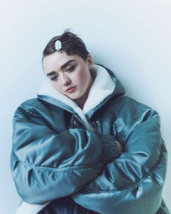 Portrait of an adult female model with short hair wearing a teal puffer jacket against a plain white background in a studio environment.