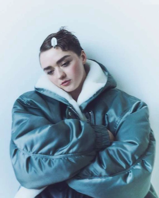 Portrait of an adult female model with short hair wearing a teal puffer jacket against a plain white background in a studio environment.