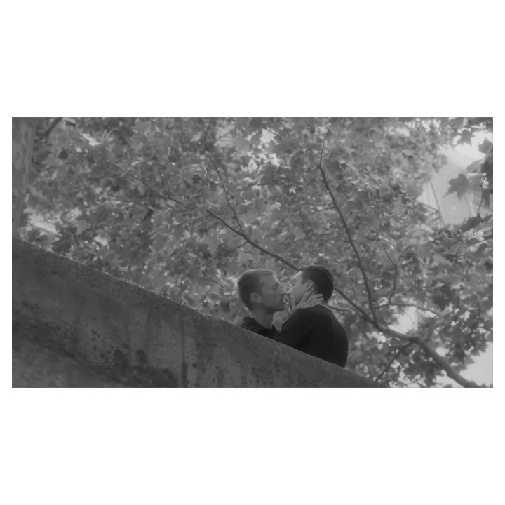 Two men kissing near a stone bridge in Paris, photographed in black and white by Amit.