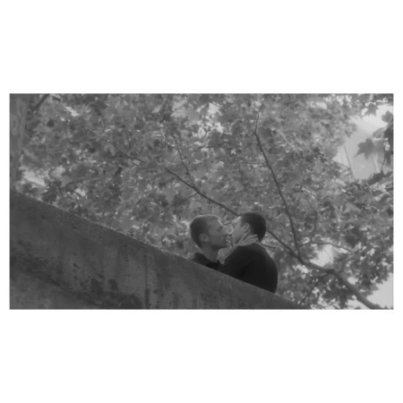 Two men kissing near a stone bridge in Paris, photographed in black and white by Amit.
