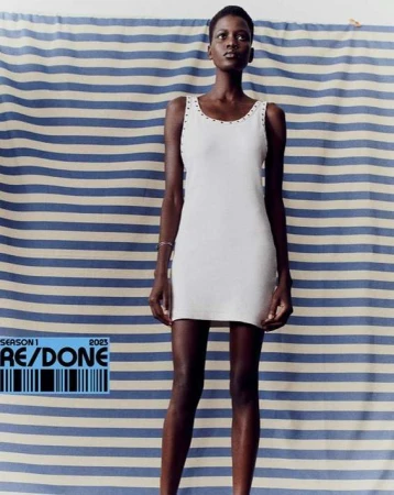 Fashion shot of Black female model in a white mini dress against a striped blue and white background. Re/Done logo with barcode visible.
