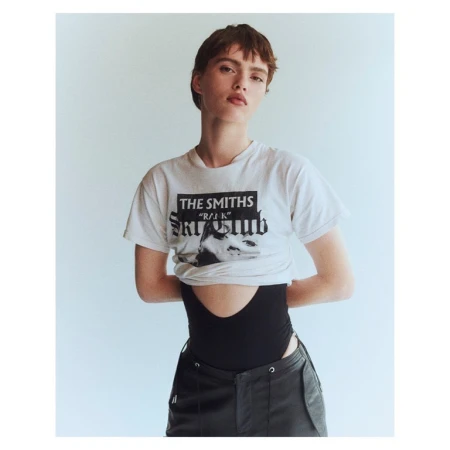 Model with short brown hair wearing a graphic white t-shirt and black pants against a seamless white background.