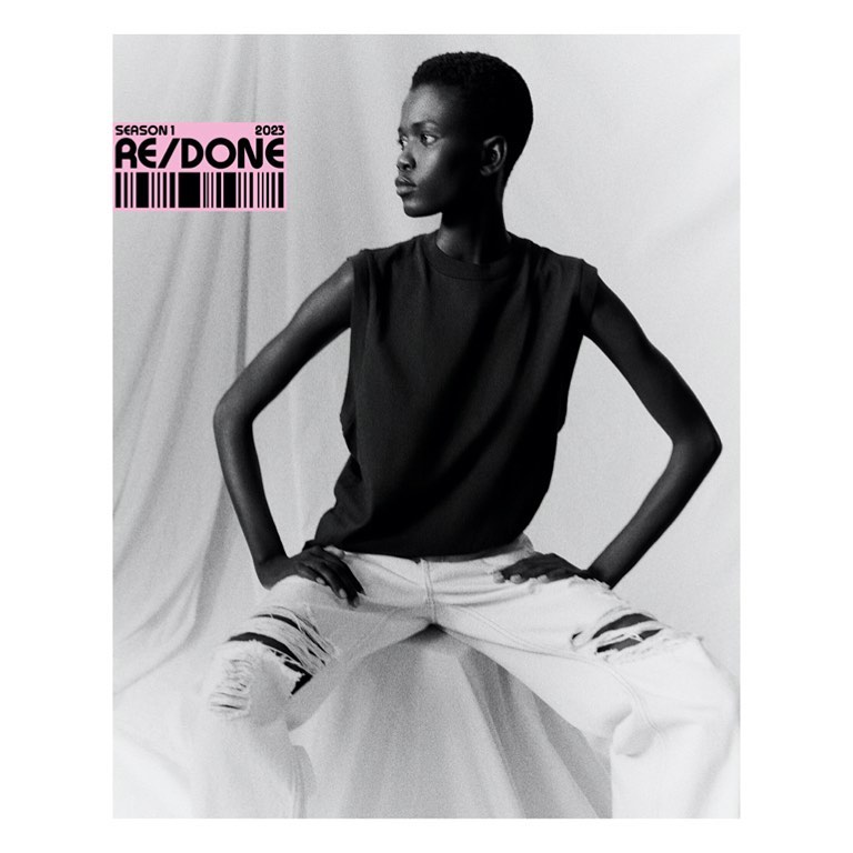 Monochrome fashion portrait of a Black woman in a sleeveless shirt and ripped jeans, posing against a white backdrop with text overlay.
