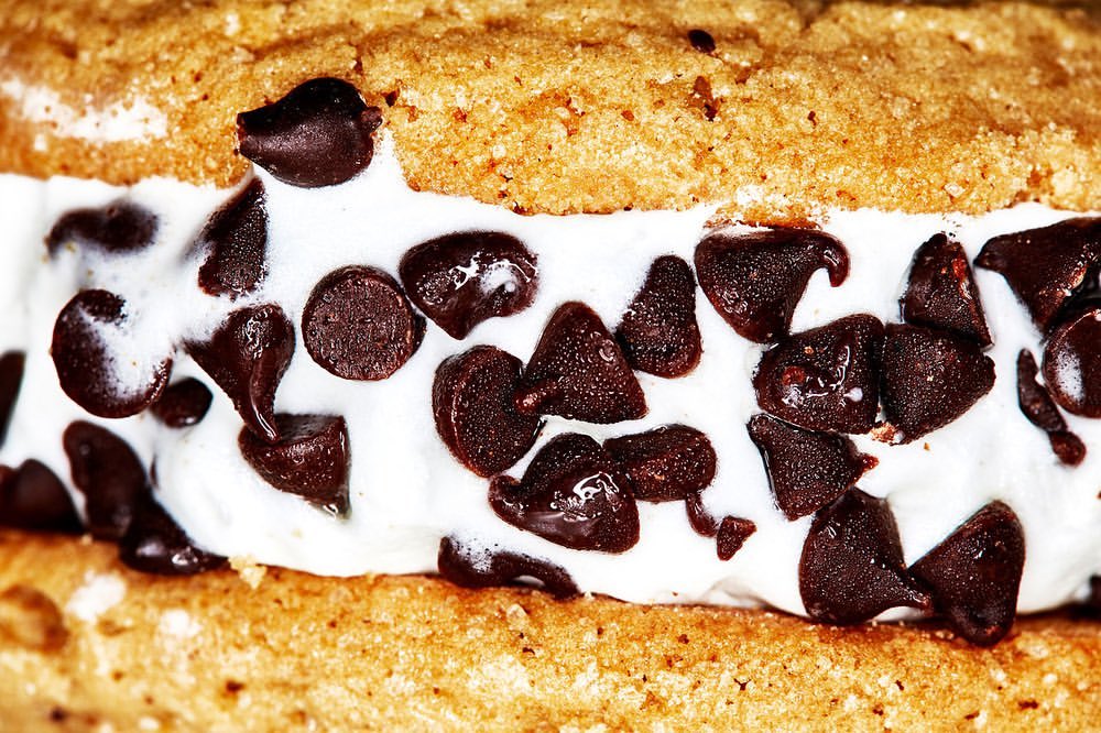 Close-up of a cookie ice cream sandwich featuring a vanilla ice cream center loaded with dark chocolate chips between two cookies.