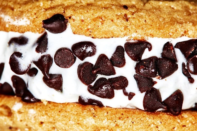 Close-up of a cookie ice cream sandwich featuring a vanilla ice cream center loaded with dark chocolate chips between two cookies.