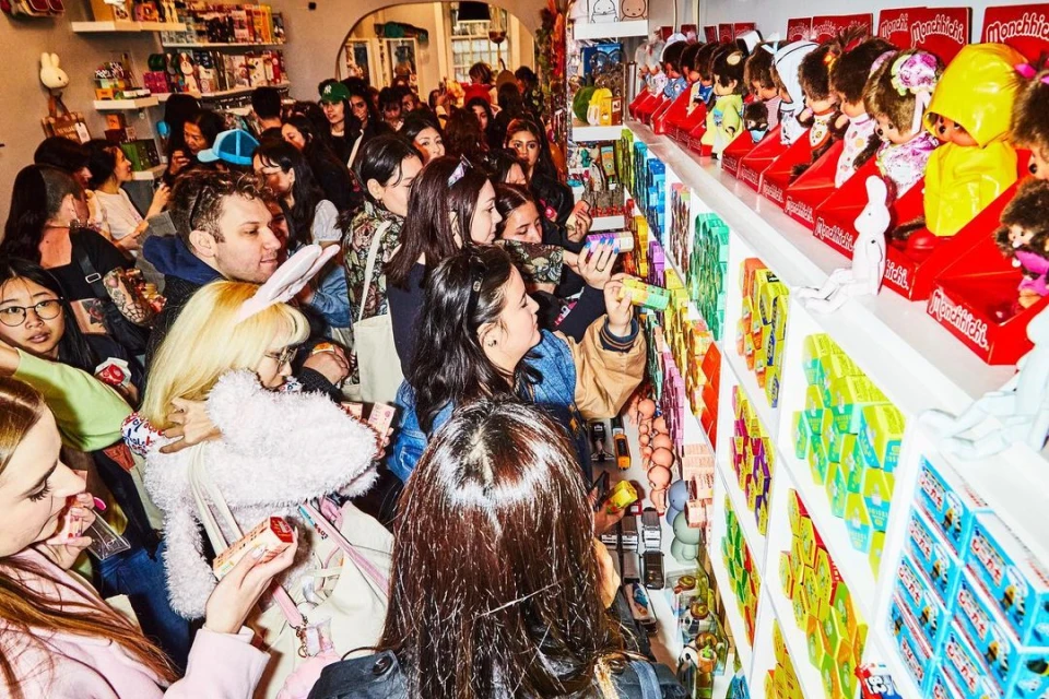 Crowd of people browsing shelves of Monchhichi dolls and other products in a retail store, creating a vibrant and busy shopping environment.