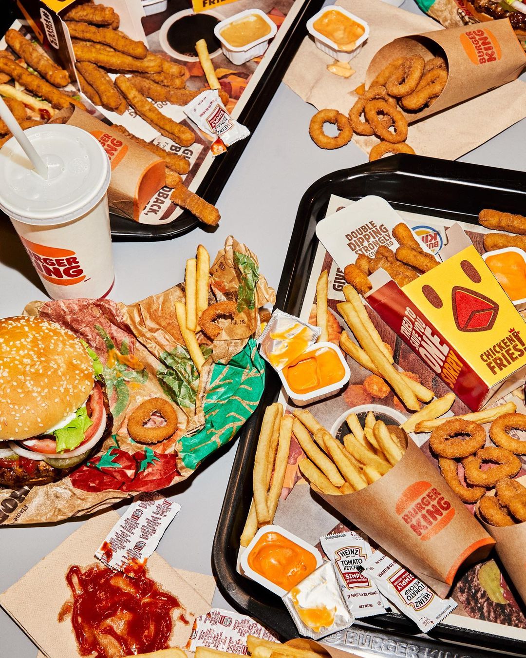 Overhead shot of Burger King fast food, including burgers, fries, onion rings, chicken fries, and dipping sauces on trays.