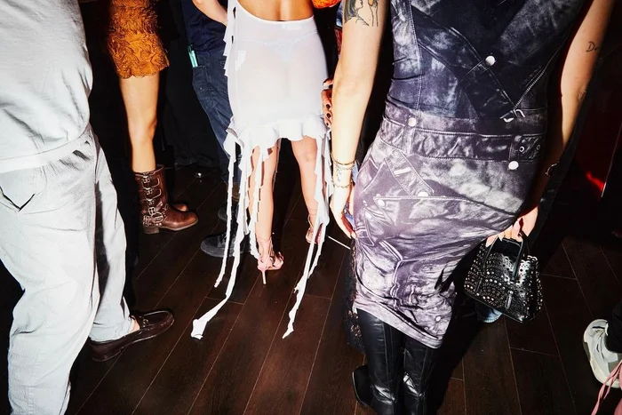Group of people dancing at a party shot from behind, showing party attire and dark wooden flooring