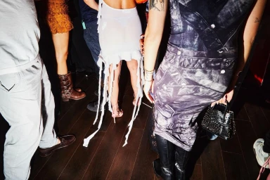 Group of people dancing at a party shot from behind, showing party attire and dark wooden flooring