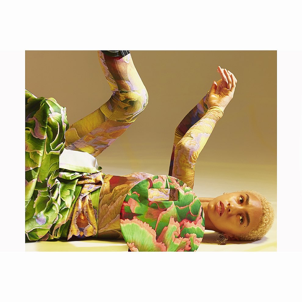 Adult female model lies down wearing colorful floral print top and leggings in a studio setting with a yellow background.