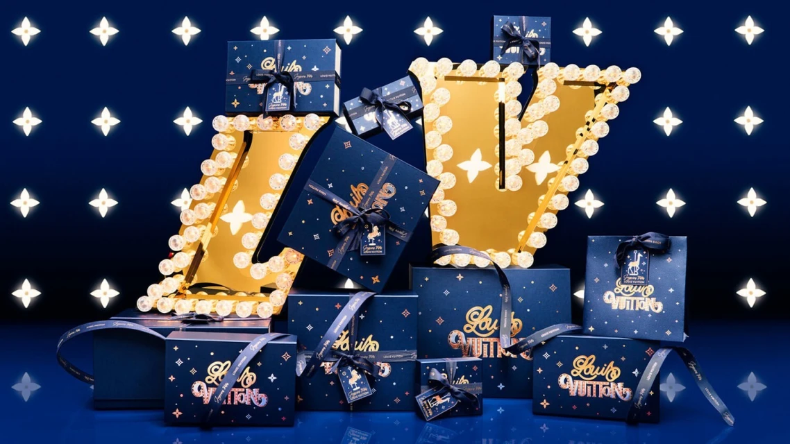 Luxury-branded gift boxes with ribbons, arranged around a gold LV monogram display against a dark blue backdrop with star pattern.