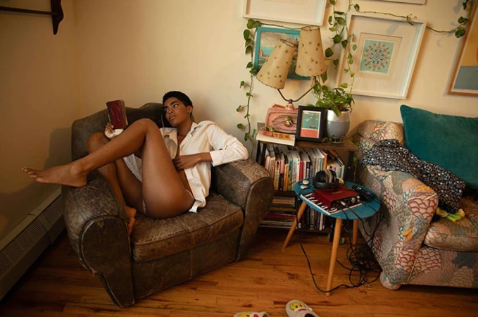 A woman in a white shirt seated in a leather armchair reading a book inside a living room, photographed by Anais Stupka.