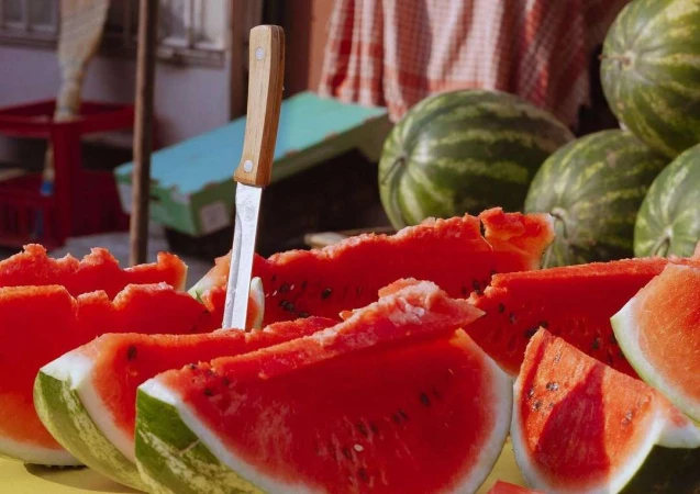 Close-up of sliced watermelon with knife in a market stall, featuring red flesh, green rind, and scattered seeds. Summer fruit still life.