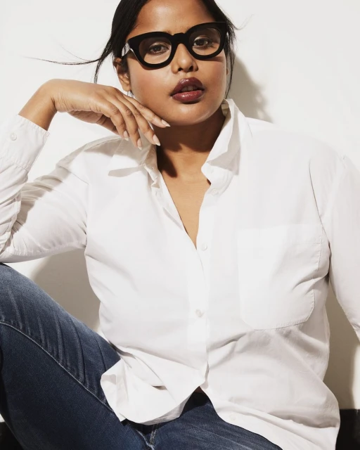 Headshot of an adult female with dark hair wearing a white button-down shirt and glasses posing in front of a white background.