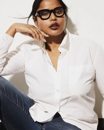 Headshot of an adult female with dark hair wearing a white button-down shirt and glasses posing in front of a white background.