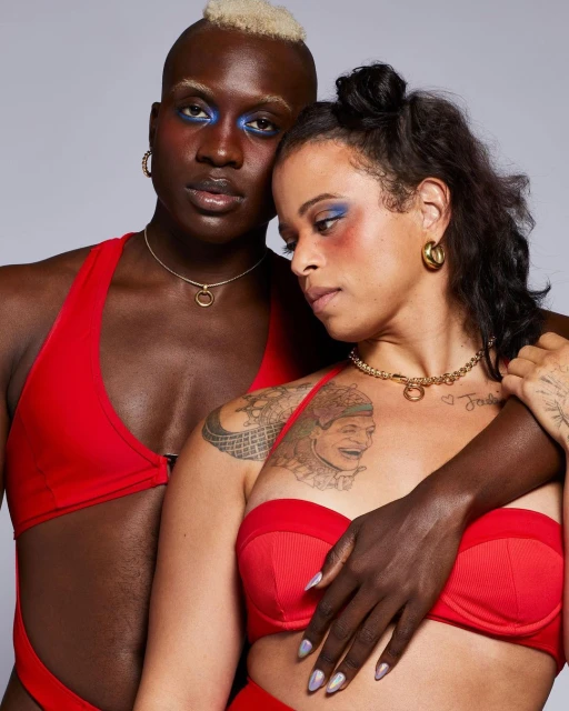 Two people in red swimwear, fashion shoot. Adult male with blonde hair, adult female with arm around male, studio setting.