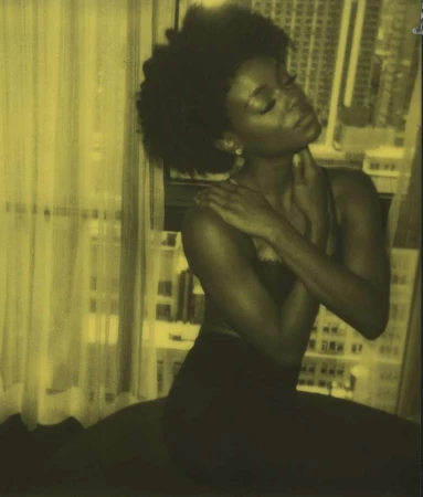 Portrait of a Black woman with natural dark hair posing near a window with sheer curtains in New York by Anastasia Garcia