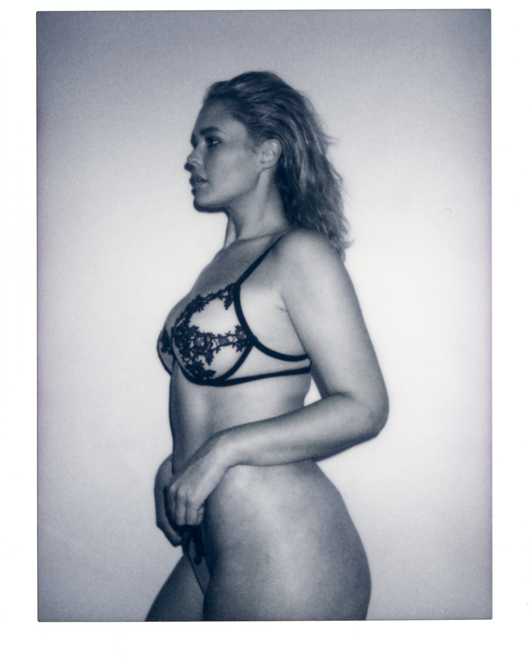 Black-and-white portrait of a woman in lingerie, captured in a photo studio, showcasing a side profile with soft, diffused lighting.