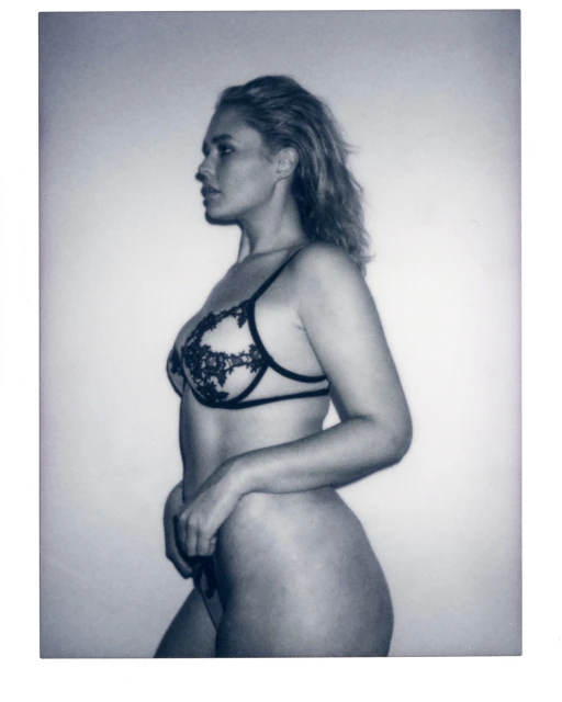 Black-and-white portrait of a woman in lingerie, captured in a photo studio, showcasing a side profile with soft, diffused lighting.