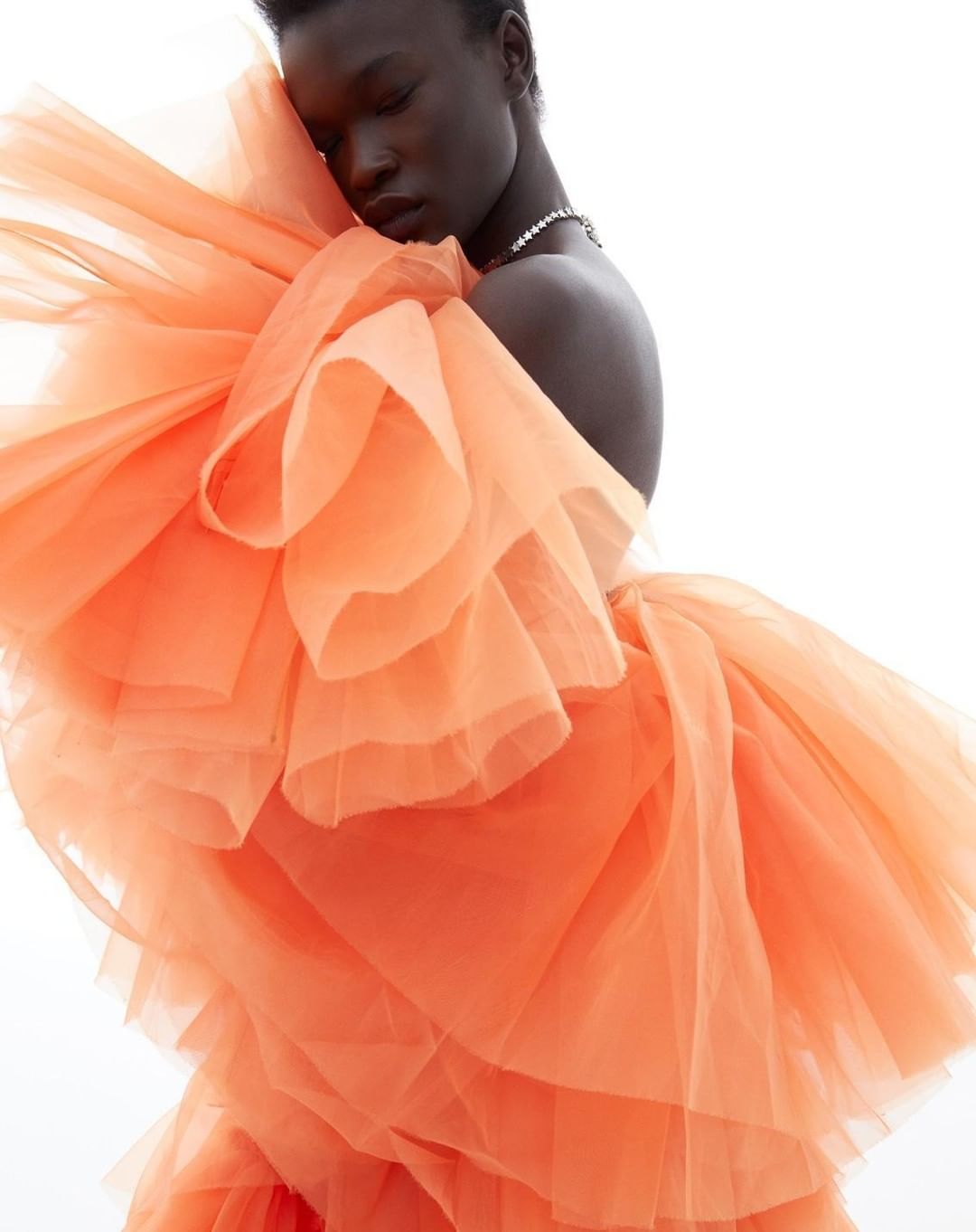 Woman in a peach-colored tulle dress with ruffles poses against a bright white background, showcasing the dress's texture and design.