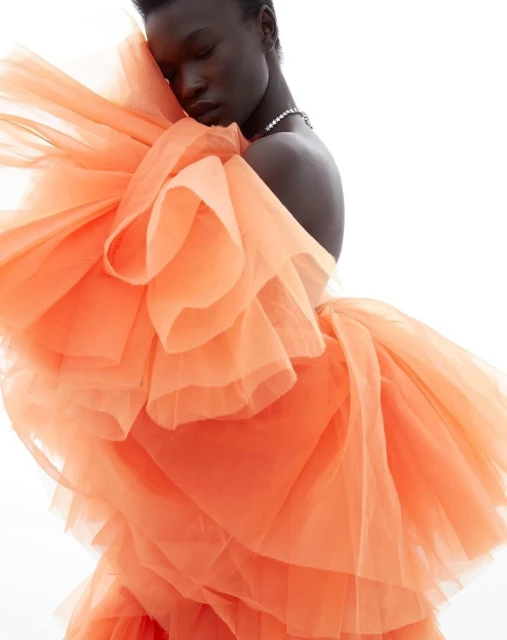 Woman in a peach-colored tulle dress with ruffles poses against a bright white background, showcasing the dress's texture and design.