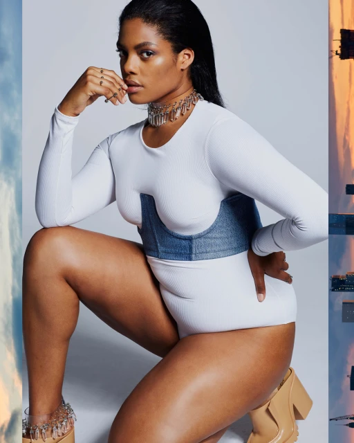 Elegant woman poses in a white bodysuit with a denim corset and nude platform shoes against a gradient studio backdrop.