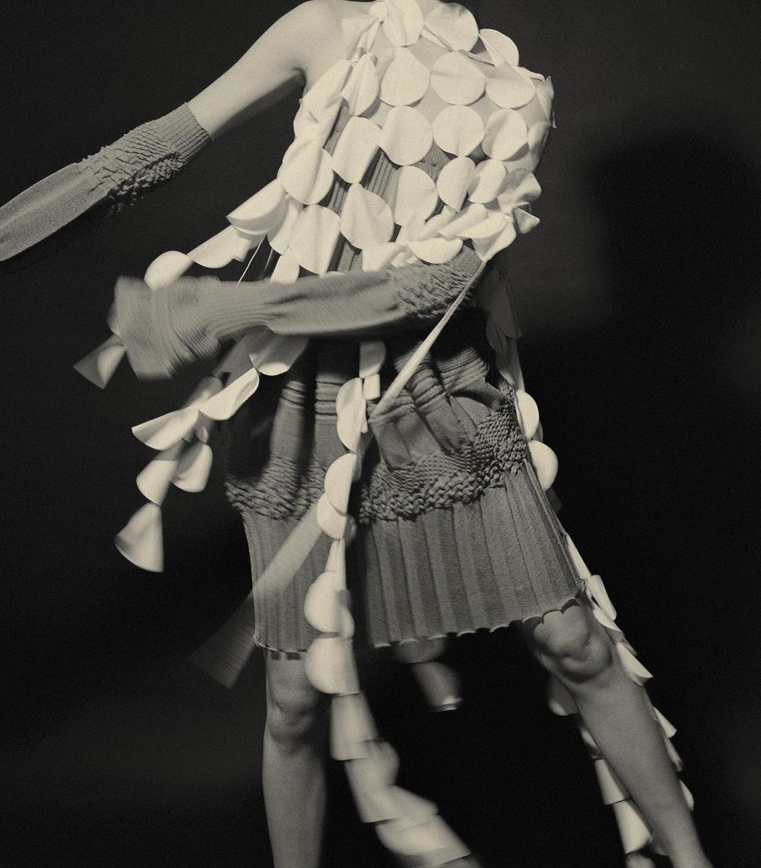 Fashion model posing in sculptural disc dress with motion blur against a dark background in a studio. Editorial fashion shot, detail.
