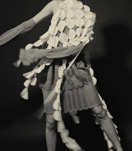 Fashion model posing in sculptural disc dress with motion blur against a dark background in a studio. Editorial fashion shot, detail.