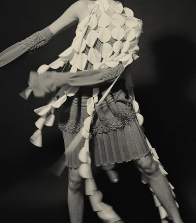 Fashion model posing in sculptural disc dress with motion blur against a dark background in a studio. Editorial fashion shot, detail.